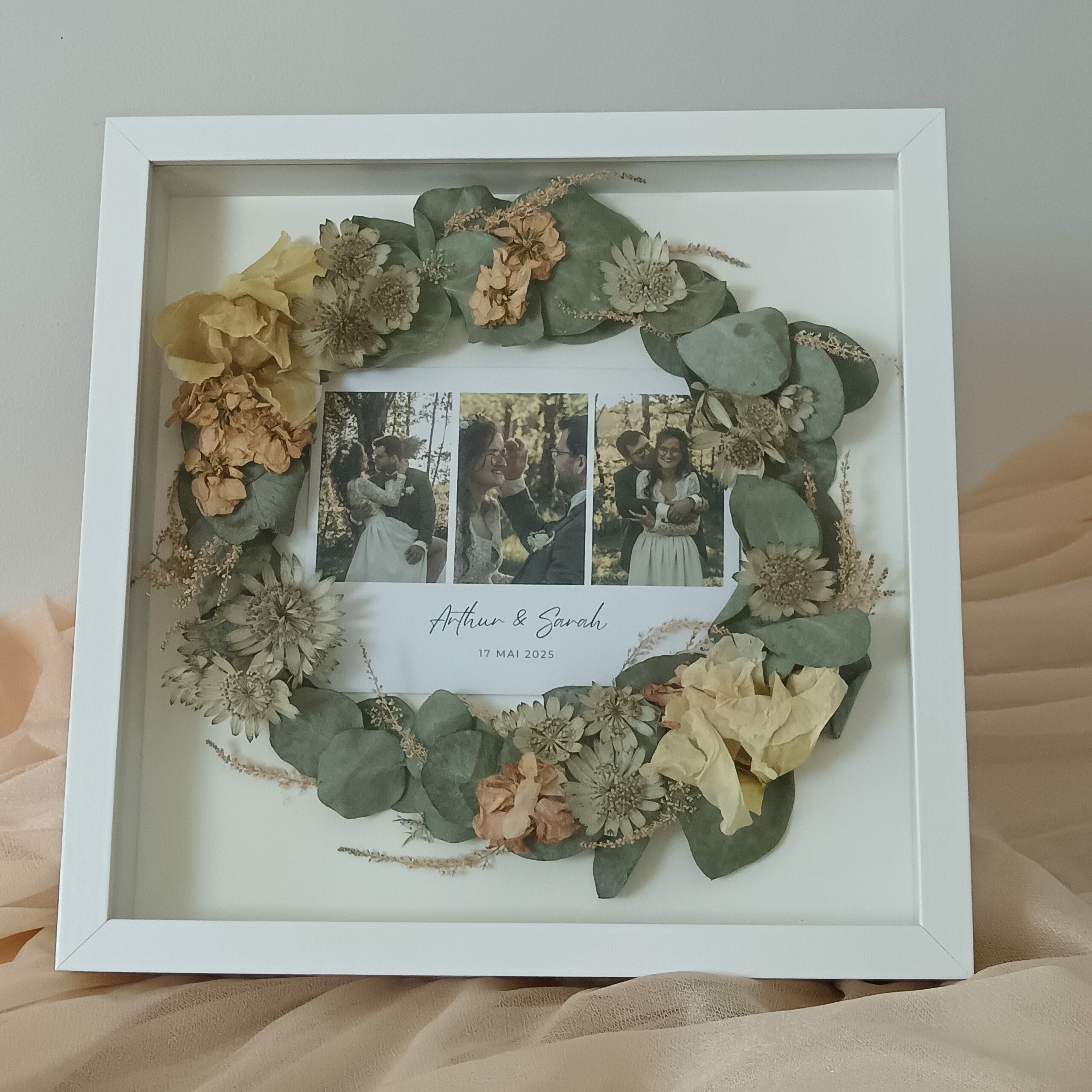Cadre souvenir de mariage avec fleurs séchées et photos du couple – création personnalisée par Invitation Florale. Conservation de bouquet de mariée en cadre rond, eucalyptus et fleurs naturelles séchées.