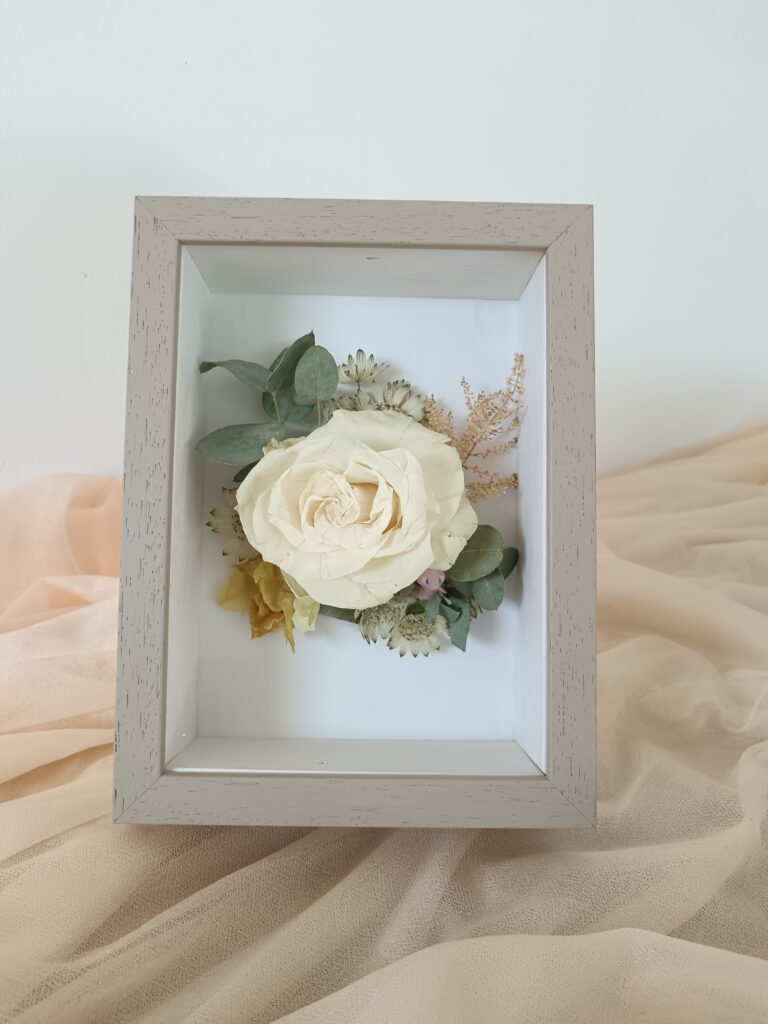 Petit cadre floral avec rose blanche préservée et feuillage d’eucalyptus, création artisanale Invitation Florale. Souvenir fleuri poétique, parfait pour un mariage ou un cadeau symbolique.